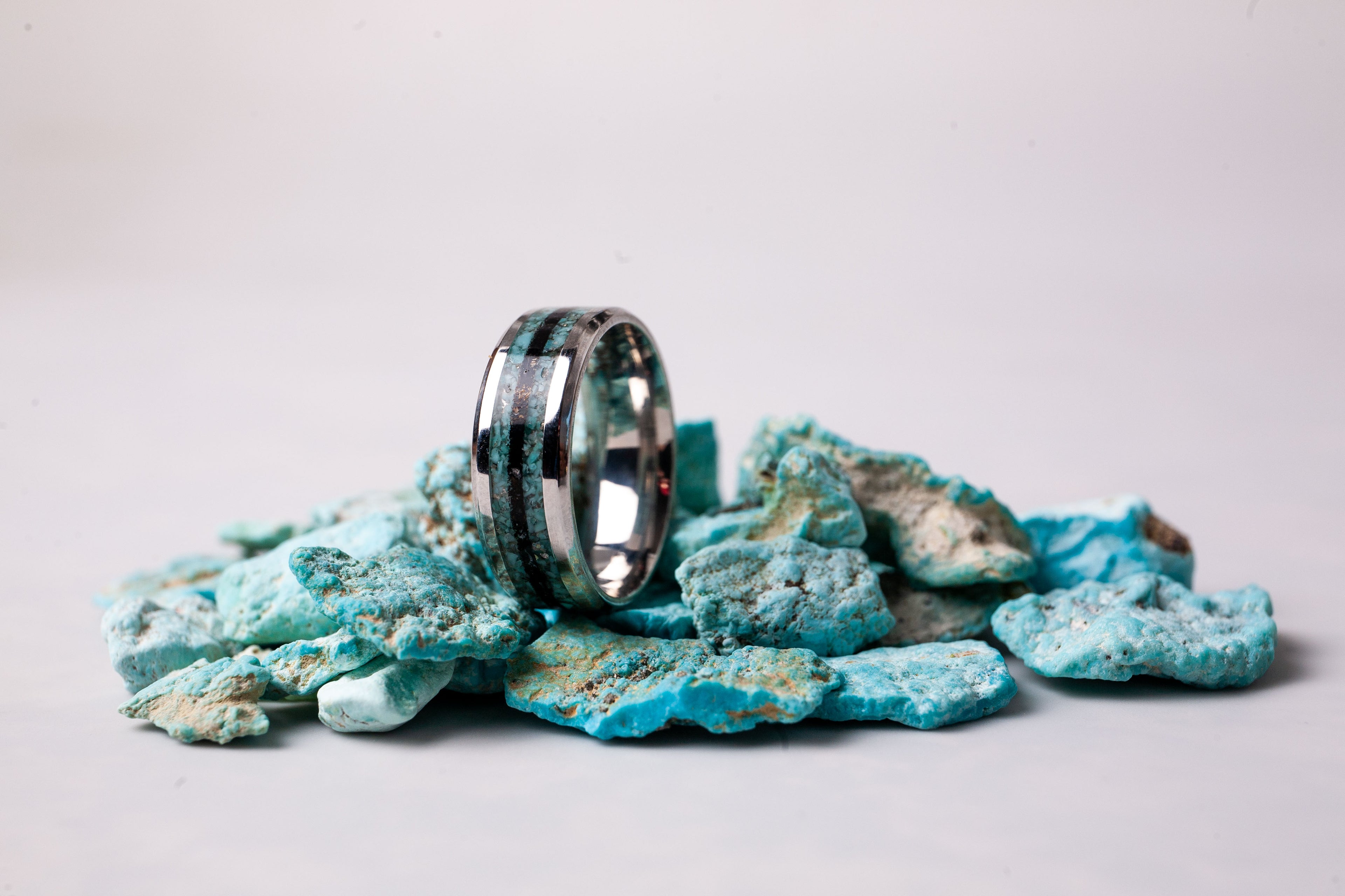Silver ring on a pile of turquoise stone-like material against a white background
